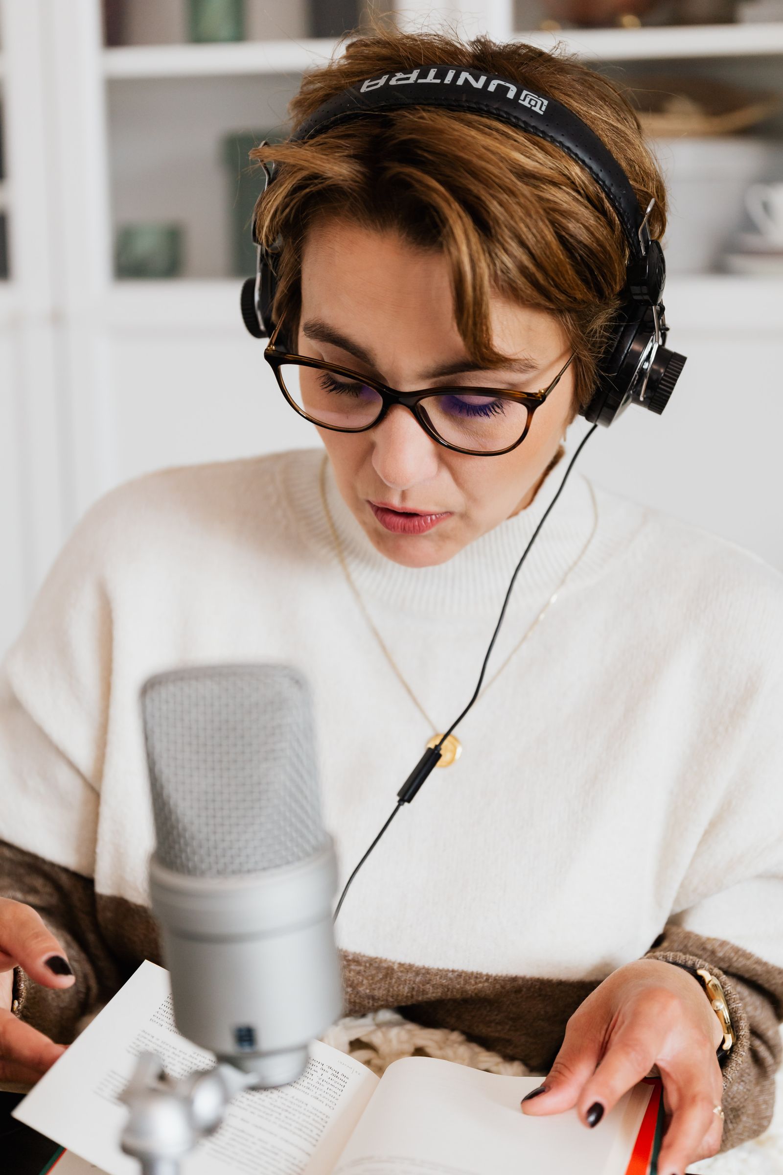 Woman wearing headphones reading aloud from a book into a microphone