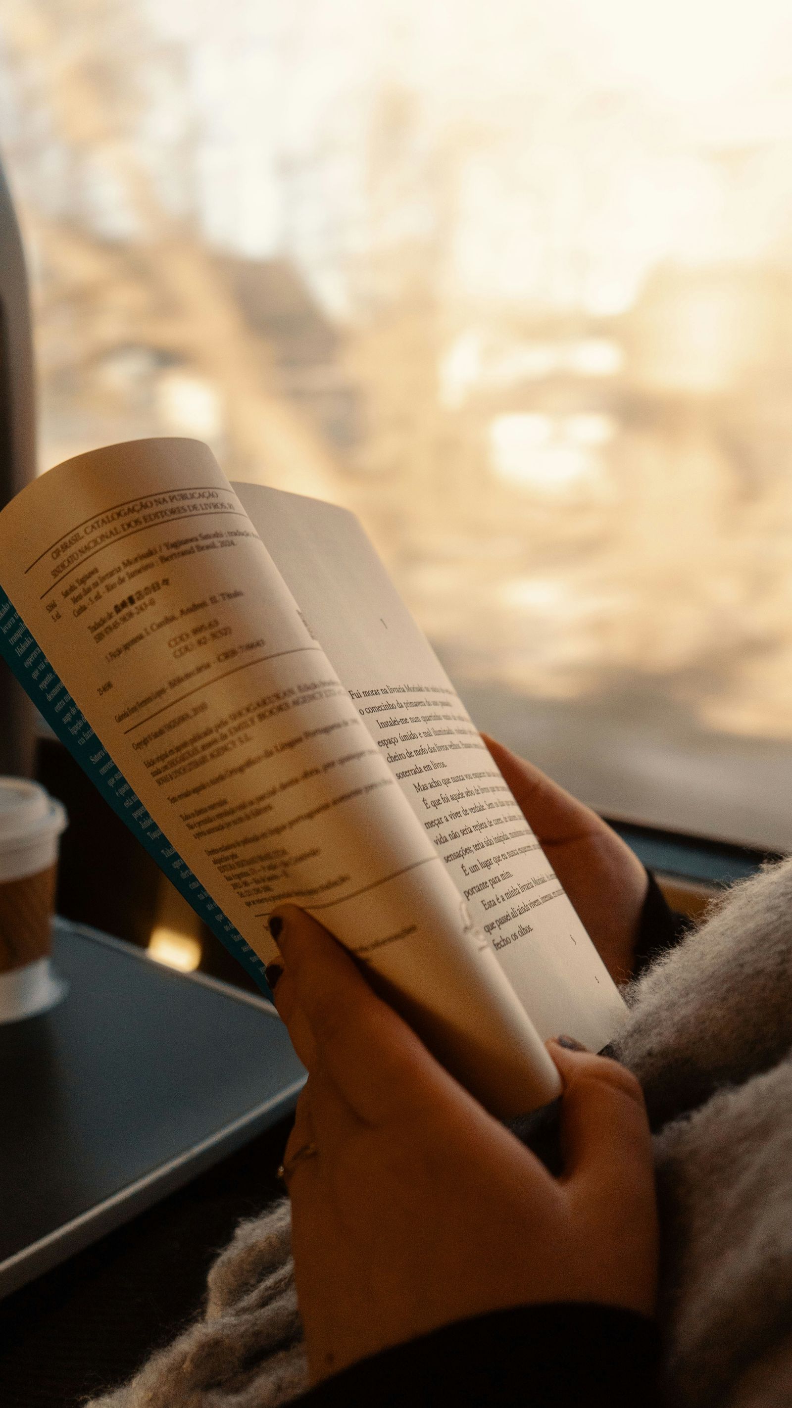 電車の中でコーヒーを手に本を読む人。通勤時間に単語を回す学び直しのイメージ