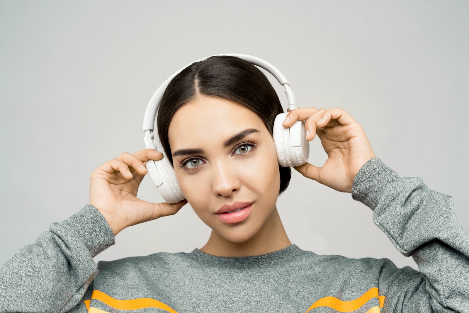 白いヘッドホンを両手で押さえ、音に耳を澄ます女性
