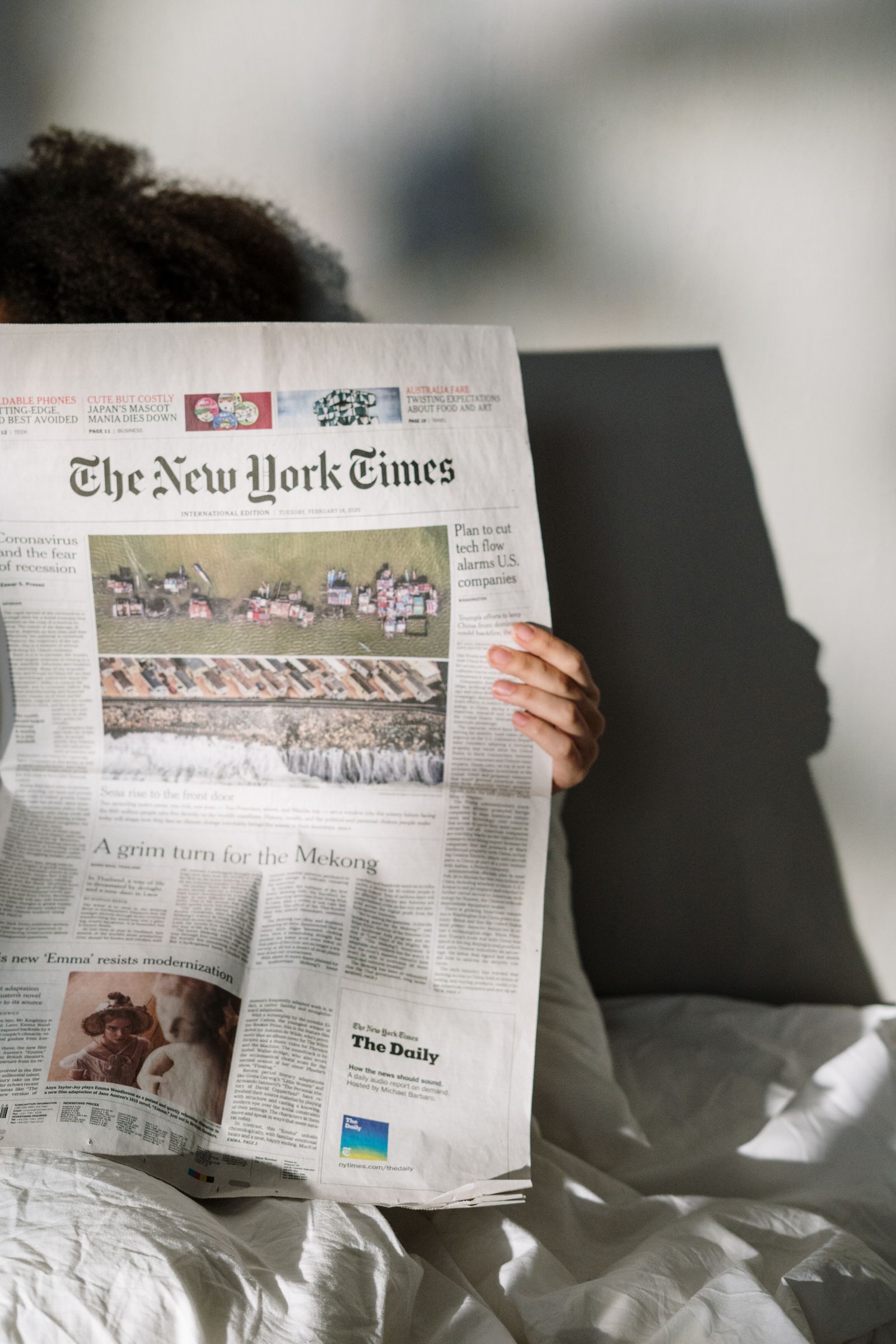 朝の光の中で英字新聞を大きく広げて読む人。ニュースの見出しで英語を学ぶイメージ