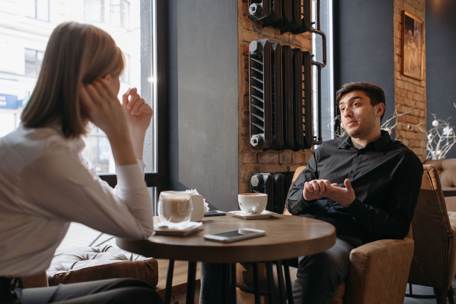 カフェでコーヒーを挟んで向かい合い、話に笑う男女。日常会話の表現を学ぶイメージ