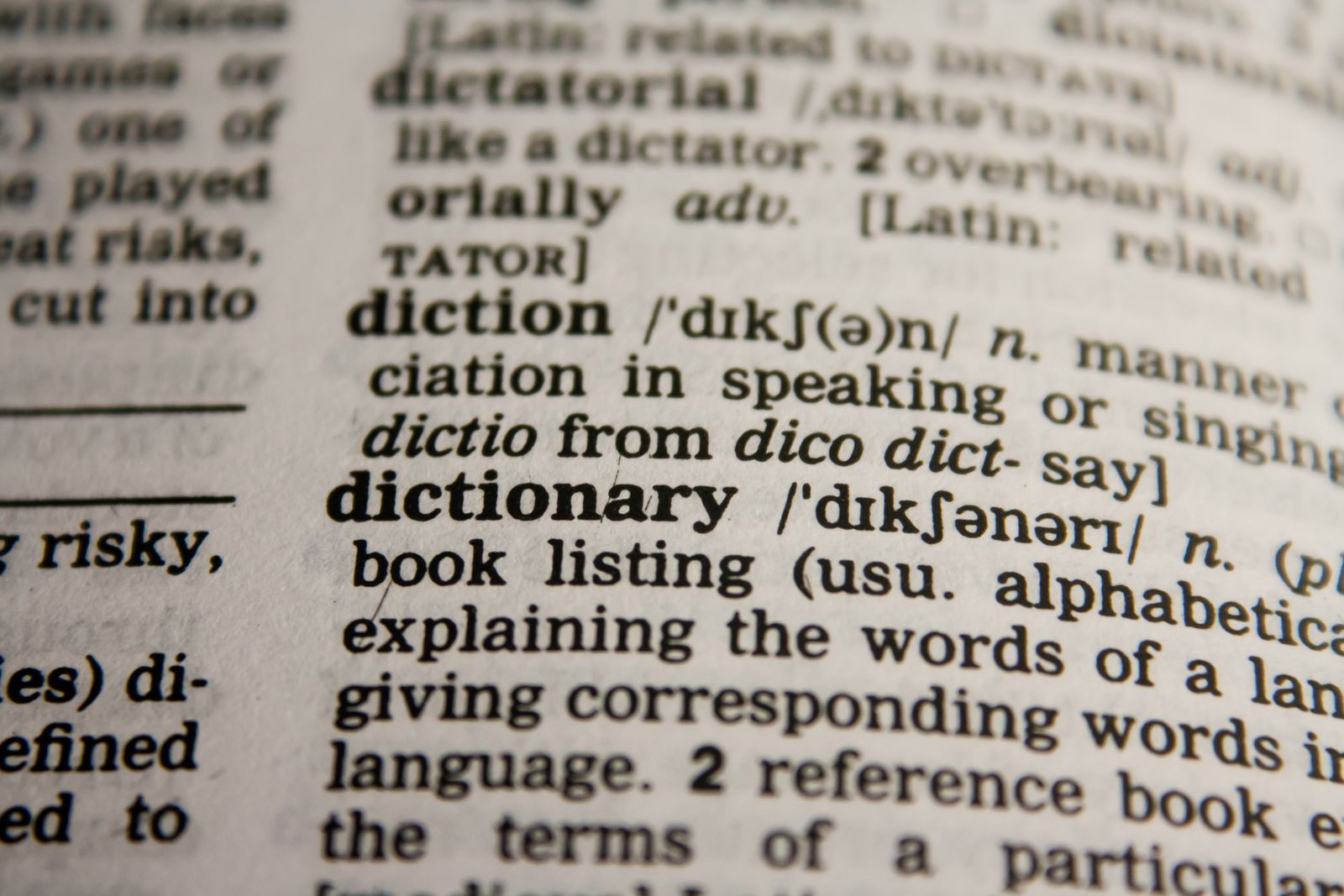英英辞典のページの接写。『dictionary』の見出し語と、ラテン語の語源を示す注記にピントが合っている。言葉の意味と由来をたどるイメージ